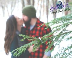 a man and woman kissing in the snow with pine needles on their forehead, surrounded by trees