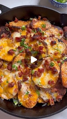 a skillet filled with cheesy potatoes covered in bacon and green onions on top of a table