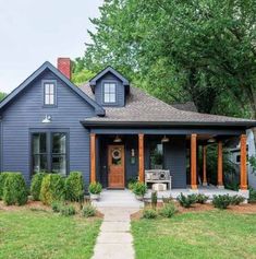 a blue house with wood trim and two front porches, surrounded by greenery