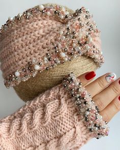 a woman's hand with red nail polish holding up a knitted hat and gloves