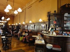 people sitting at tables in a restaurant with chandeliers hanging from the ceiling