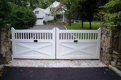 a white gate in front of a house with stone walls and trees around the entrance