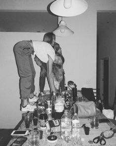 black and white photograph of two people bending over a table full of liquor bottles on it