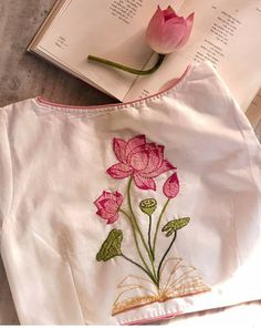 a white shirt with pink flowers on it next to an open book and a flower