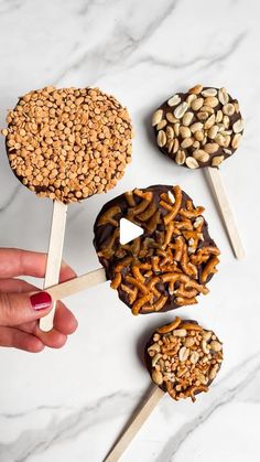 hand holding pops with pretzels and nuts on them in front of white marble counter top