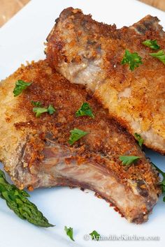 two pieces of meat sitting on top of a white plate with asparagus sprouts