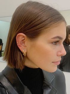 a woman in a black leather jacket is looking at her cell phone and wearing gold earrings