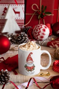 a cup of hot chocolate with whipped cream and santa clause on it, surrounded by christmas decorations