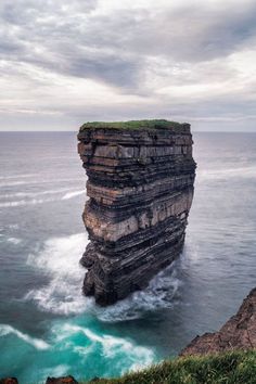 a large rock sticking out of the ocean next to a cliff with waves crashing on it