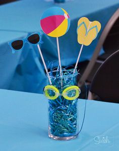 a vase filled with blue plastic straws and beach ball decorations on top of a table