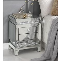 a mirrored nightstand with two drawers and flowers on the top, next to a bed