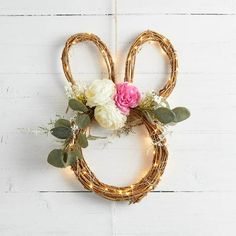 a rattan wreath with flowers and greenery hanging on a white wooden wall in the shape of a rabbit's head