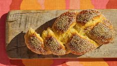 four loaves of bread sitting on top of a wooden cutting board next to an orange and pink table cloth