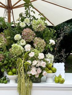 an arrangement of flowers, fruit and vegetables on a table with an umbrella in the background