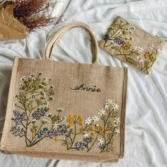 two embroidered bags sitting on top of a bed next to each other with flowers in them