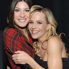 two beautiful women hugging each other in front of a black background and one is wearing a red plaid shirt