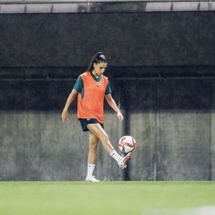 a woman kicking a soccer ball on top of a field