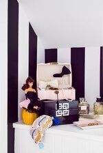 a room with black and white stripes on the walls, two dolls sitting in suitcases