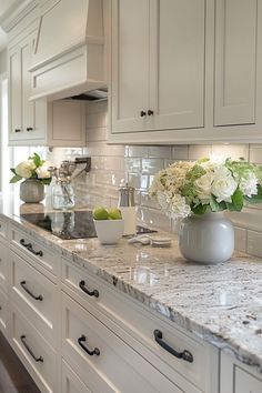 a kitchen with white cabinets and marble counter tops, vases filled with flowers on the island