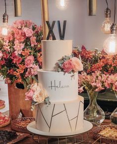 a three tiered wedding cake with flowers on the top is displayed in front of other desserts