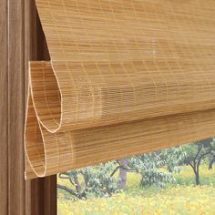 a close up of a bamboo blind in front of a window with trees and yellow flowers