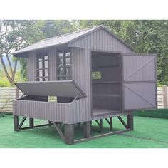 a gray chicken coop with an open door on the side and green grass around it