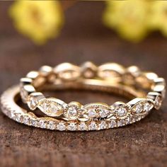 two gold wedding bands with white diamonds on wooden table next to yellow flowers and petals