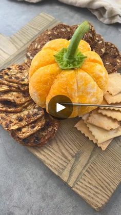 a wooden cutting board topped with crackers and an orange on top of bread slices