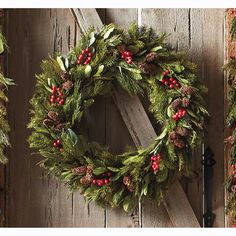 a wreath is hanging on the side of a wooden door with pine cones and berries