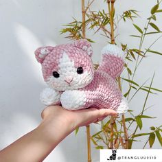 a hand holding a pink and white crocheted cat