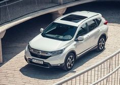 a white honda cr - v is parked in front of a bridge on a brick walkway