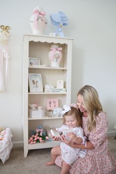 a woman holding a baby next to a white bookcase with pink and blue decorations