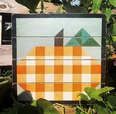 an orange and white checkered patchwork quilt sitting on top of a wooden fence