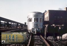 two men standing next to a silver train on the tracks in an old time photo