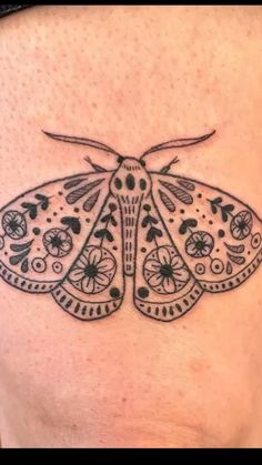 a black and white moth tattoo on the back of a woman's stomach,