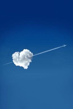 an airplane is flying in the blue sky with a cloud shaped like a heart on it's tail