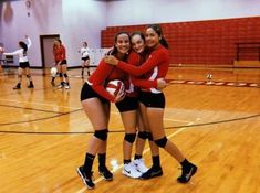 three girls in red and black uniforms hugging each other on a basketball court with their arms around one another