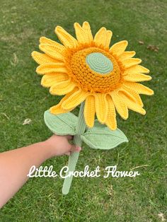 a crocheted sunflower is being held by someone's hand in the grass