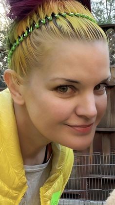 a woman with blonde hair wearing a yellow jacket and green headband smiling at the camera