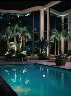 an indoor swimming pool at night with palm trees and lounge chairs around the pool area