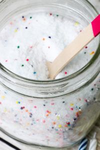 a wooden spoon sticking out of a jar filled with white sugar and sprinkles