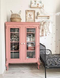 a pink china cabinet with glass doors in a white walled room next to a bed