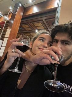 a man and woman holding wine glasses in front of their faces while posing for the camera