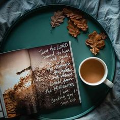 an open book and cup of coffee on a green plate with leaves next to it