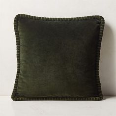 a green velvet pillow with ruffled edges on a white surface, against a wall