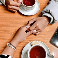 two people sitting at a table holding hands with cups of tea in front of them