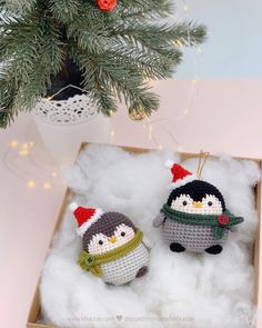 two crocheted penguin ornaments in a box next to a christmas tree