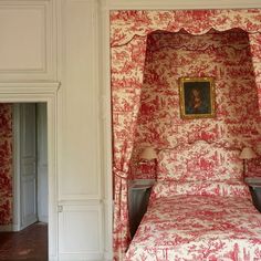 a bed with red and white wallpaper in a room next to a painting on the wall