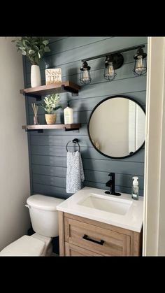 a white toilet sitting under a bathroom mirror next to a wooden sink vanity with shelves above it