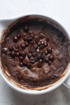 a white bowl filled with chocolate chips and brownie batter on top of a table